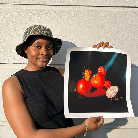 artist holding printed image of tomatoes, tatashe peppers and scotch bonnet peppers